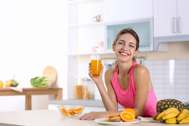 Woman with glass of orange juice at table in kitchen. Healthy diet