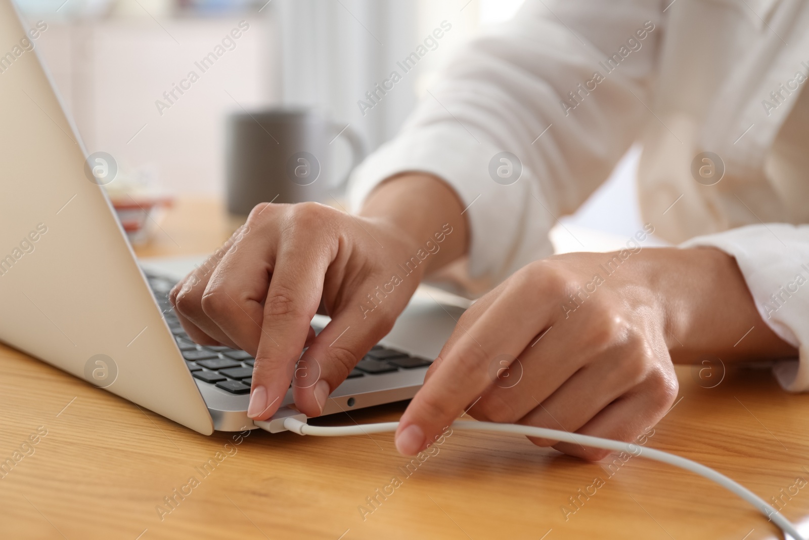 Photo of Woman connecting charger cable to laptop at wooden table, closeup