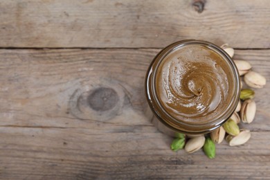 Photo of Tasty pistachio nut paste in jar on wooden table, top view. Space for text