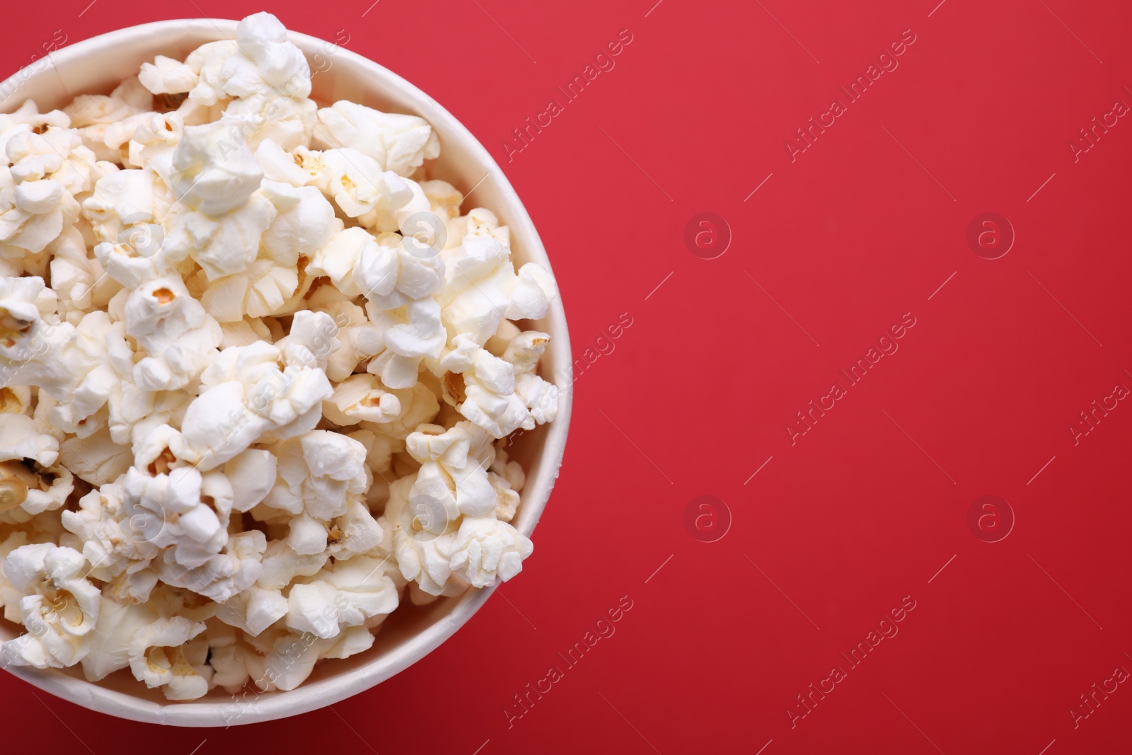 Photo of Paper bucket with delicious popcorn on red background, top view. Space for text