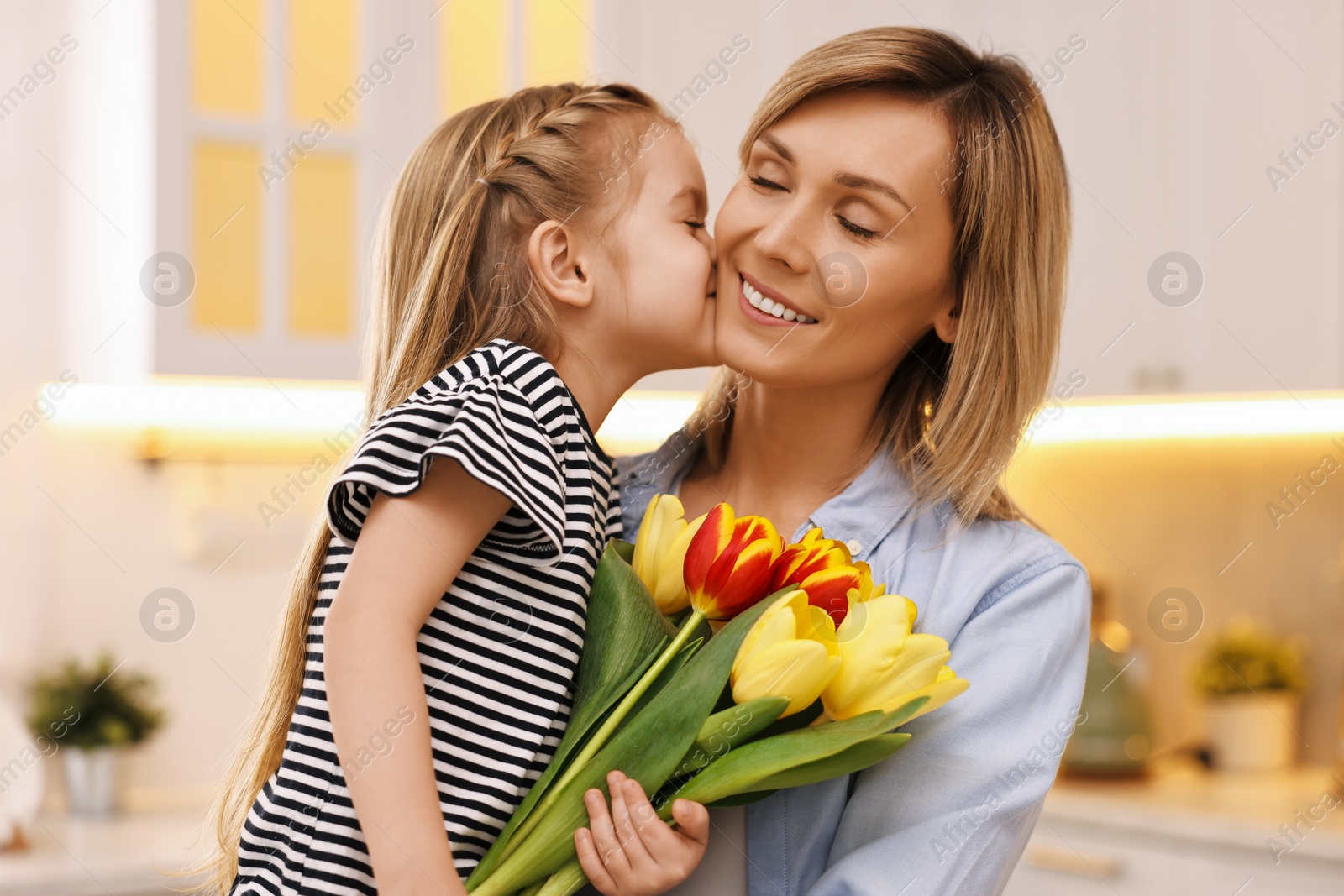 Photo of Little daughter kissing and congratulating her mom with Mother`s Day at home. Woman holding bouquet of beautiful tulips