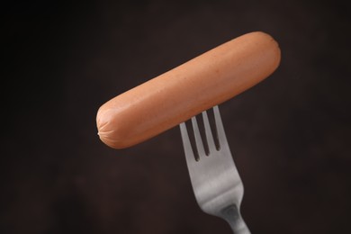 Photo of Delicious boiled sausage on fork against dark background, closeup