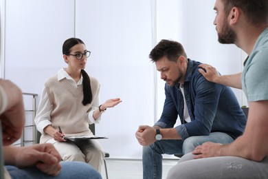 Psychotherapist working with group of drug addicted people at therapy session indoors