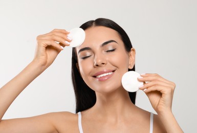 Photo of Young woman using cotton pads with micellar water on light grey background