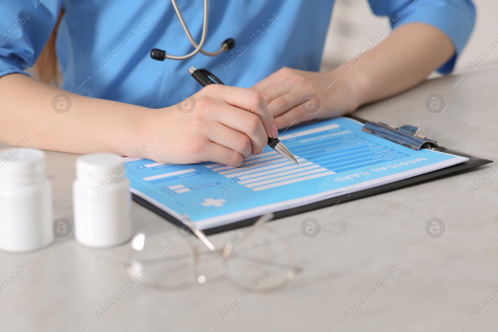 Photo of Doctor filling patient's medical card at table in clinic, closeup