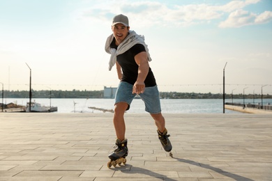 Handsome young man roller skating on pier near river