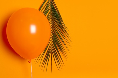 Orange balloon and palm leaf on color background. Celebration time