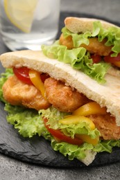 Photo of Delicious pita sandwiches with fried fish, pepper, tomatoes and lettuce on dark grey table, closeup