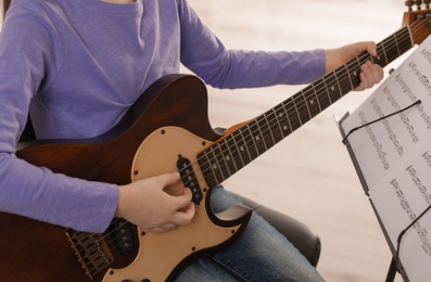 Child playing guitar at music lesson, closeup. Learning notes