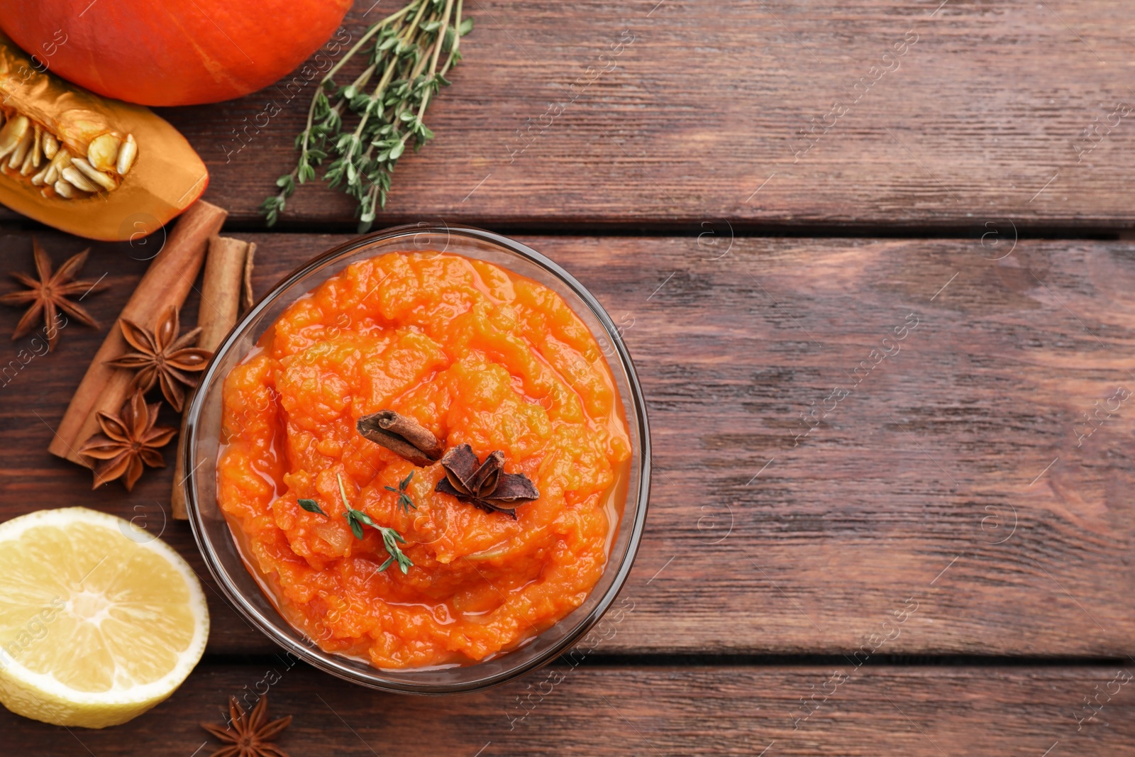 Photo of Bowl of delicious pumpkin jam and ingredients on wooden table, flat lay. Space for text