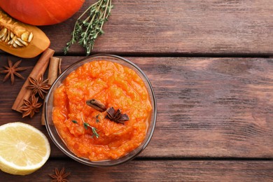 Photo of Bowl of delicious pumpkin jam and ingredients on wooden table, flat lay. Space for text
