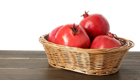 Photo of Fresh pomegranates in wicker basket on wooden table against white background