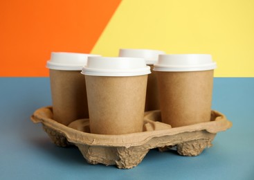 Takeaway paper coffee cups with plastic lids in cardboard holder on color background