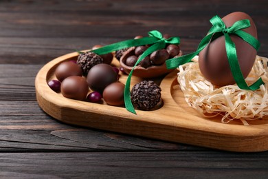Photo of Tasty chocolate eggs with green bows and sweets on wooden table