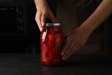 Photo of Woman pickling glass jar of tomatoes at black kitchen table, closeup