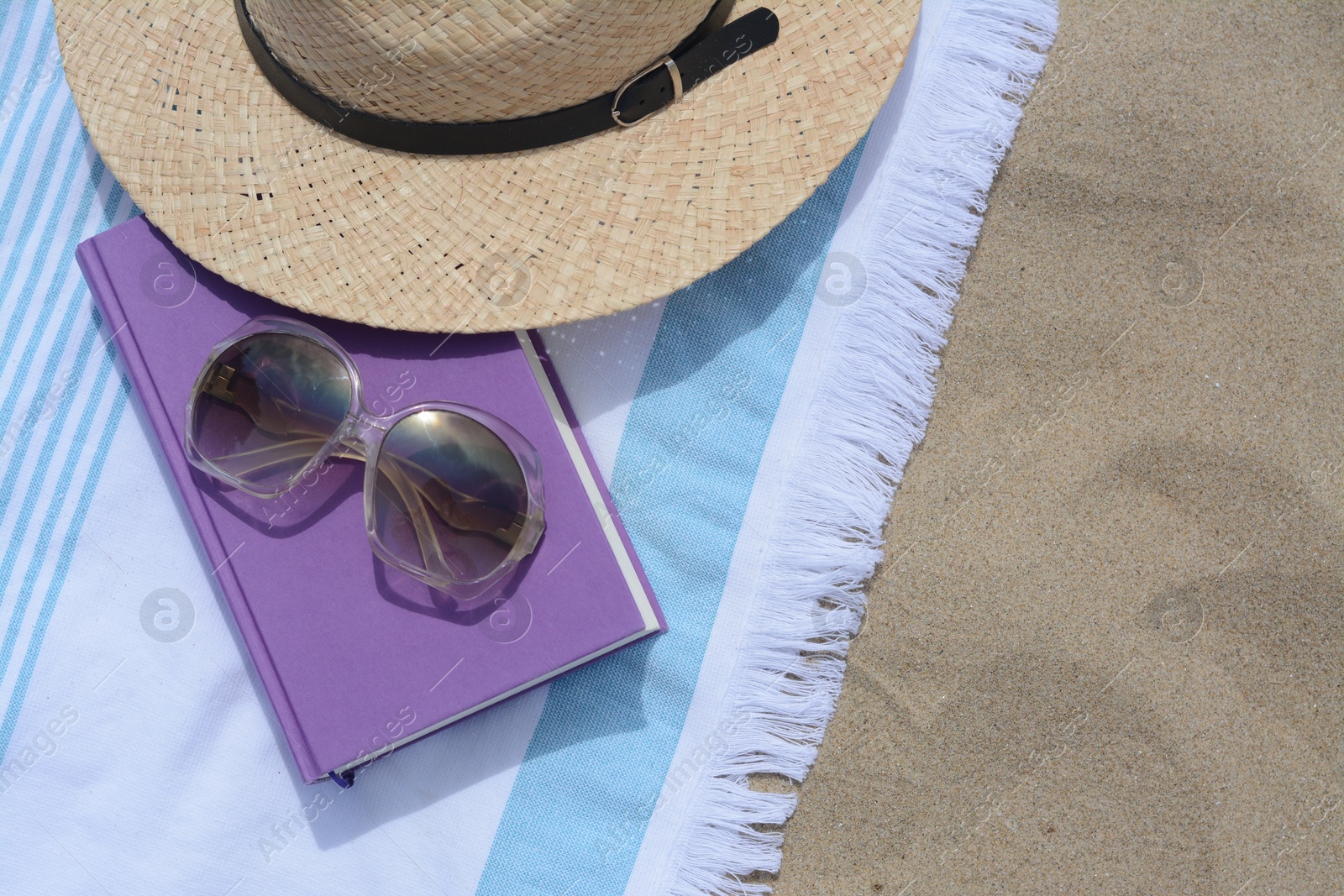 Photo of Beach towel with book, sunglasses and straw hat on sand, flat lay. Space for text