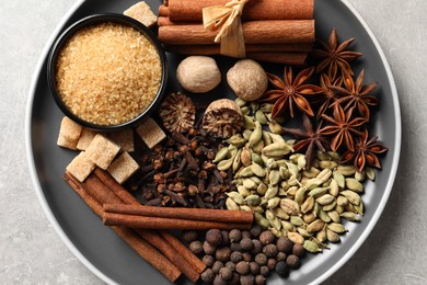 Plate with different aromatic spices on light textured table, top view