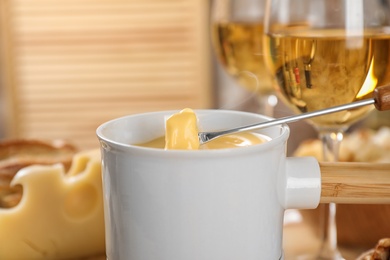 Photo of Pot of tasty cheese fondue and fork with bread on table