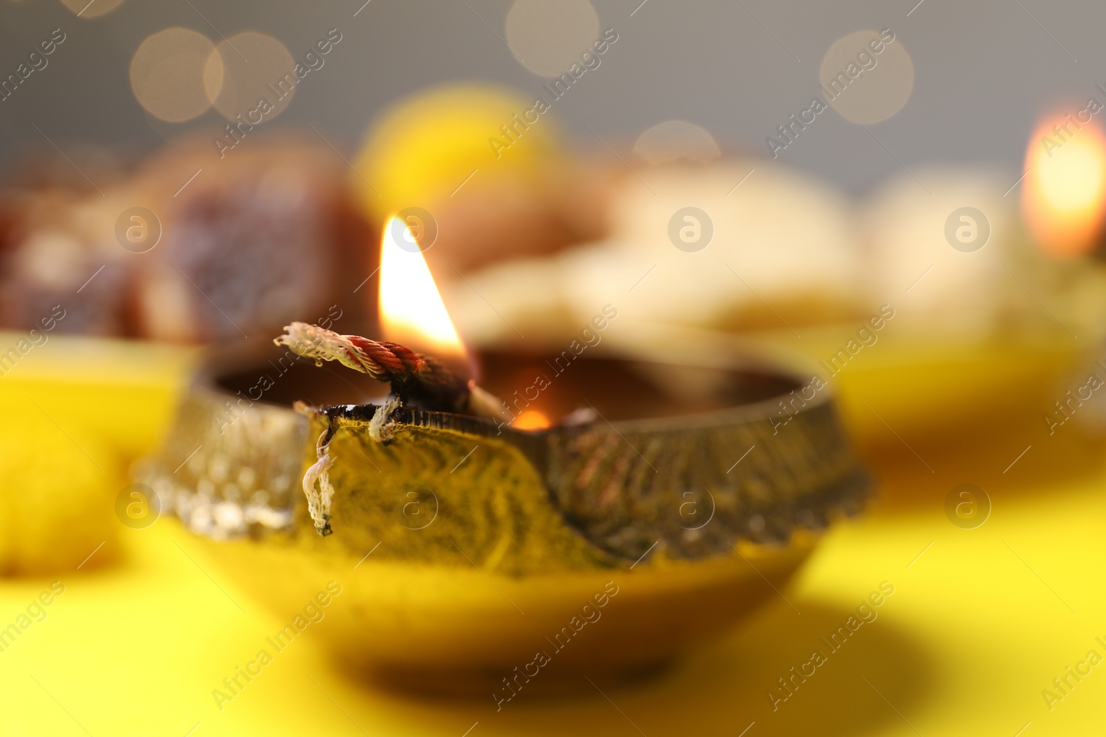 Photo of Happy Diwali. Diya lamp on yellow table against blurred lights, closeup