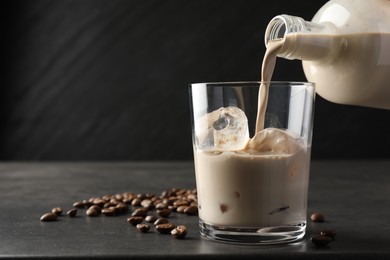 Photo of Pouring coffee cream liqueur into glass at grey table, closeup. Space for text