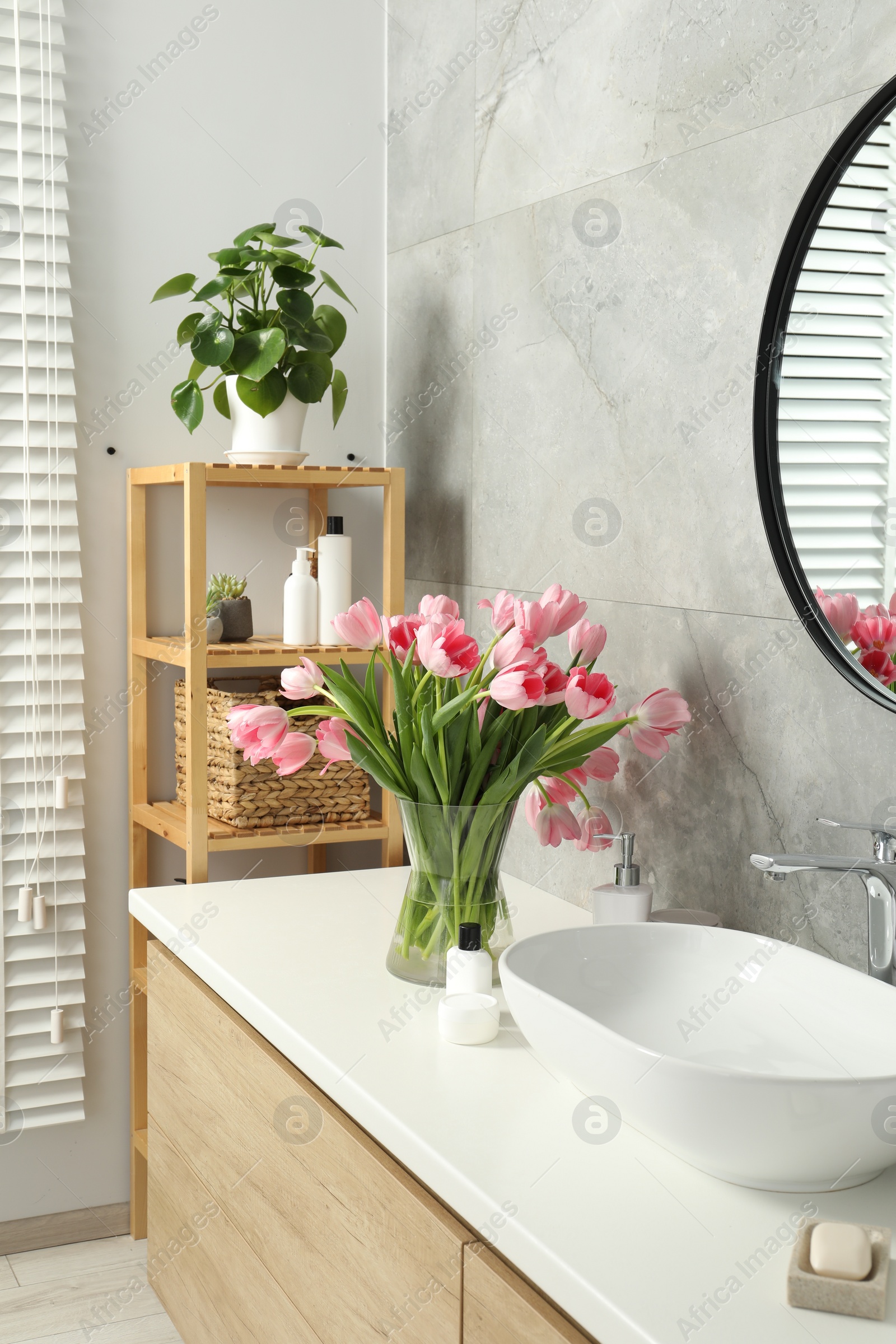 Photo of Vase with beautiful pink tulips and toiletries near sink in bathroom