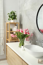 Vase with beautiful pink tulips and toiletries near sink in bathroom