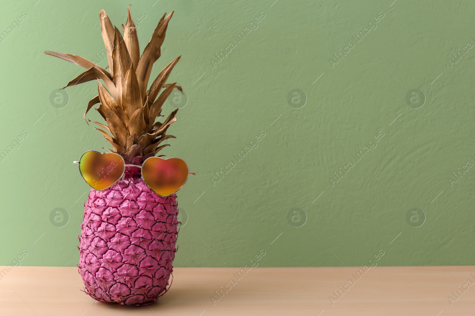 Photo of Pink pineapple with sunglasses on table against color wall