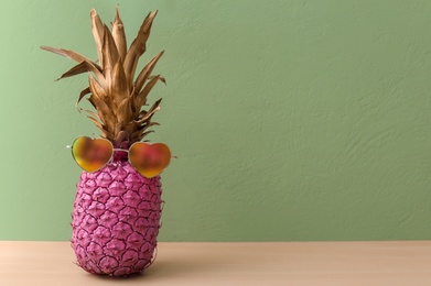 Photo of Pink pineapple with sunglasses on table against color wall