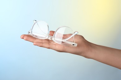 Photo of Woman holding glasses with transparent frame on color background, closeup