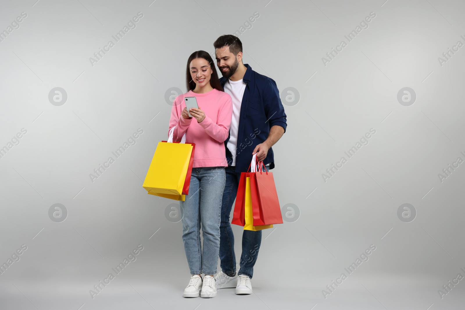 Photo of Happy couple with shopping bags and smartphone on grey background
