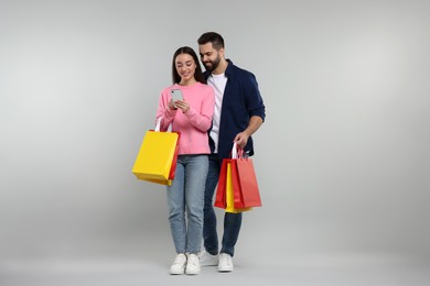 Happy couple with shopping bags and smartphone on grey background