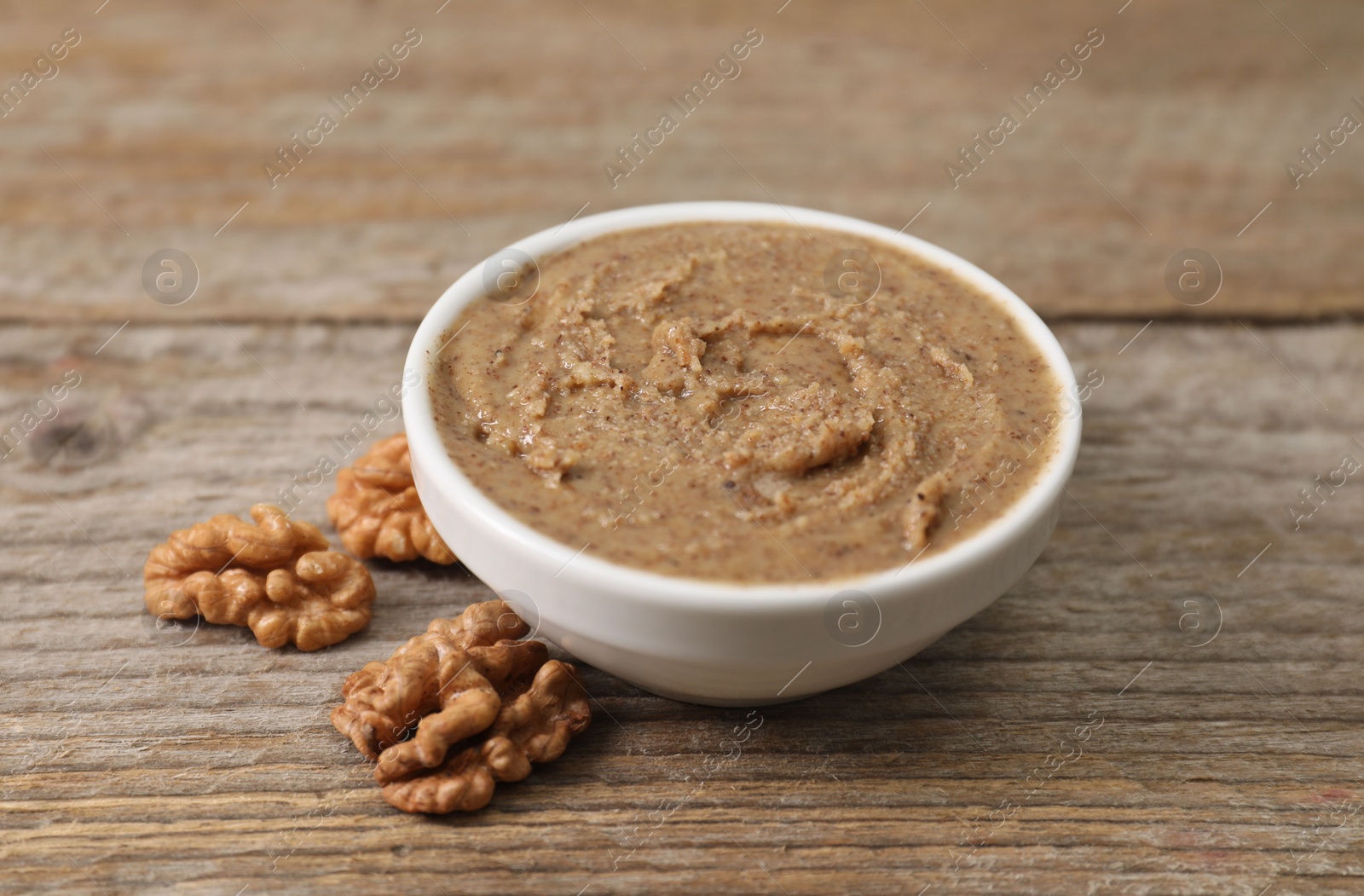 Photo of Delicious nut butter in bowl and walnuts on wooden table, closeup