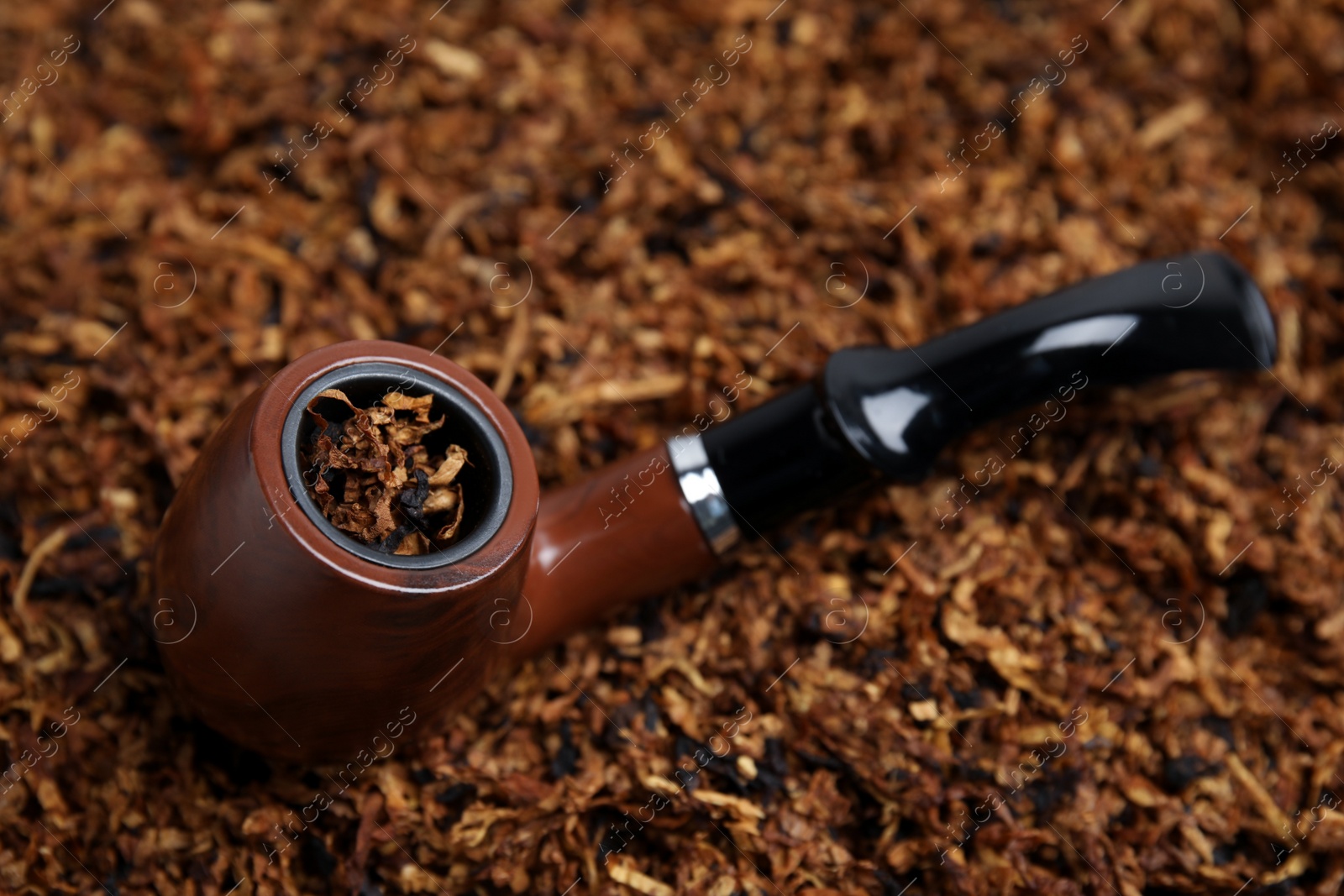 Photo of Smoking pipe on pile of tobacco, closeup