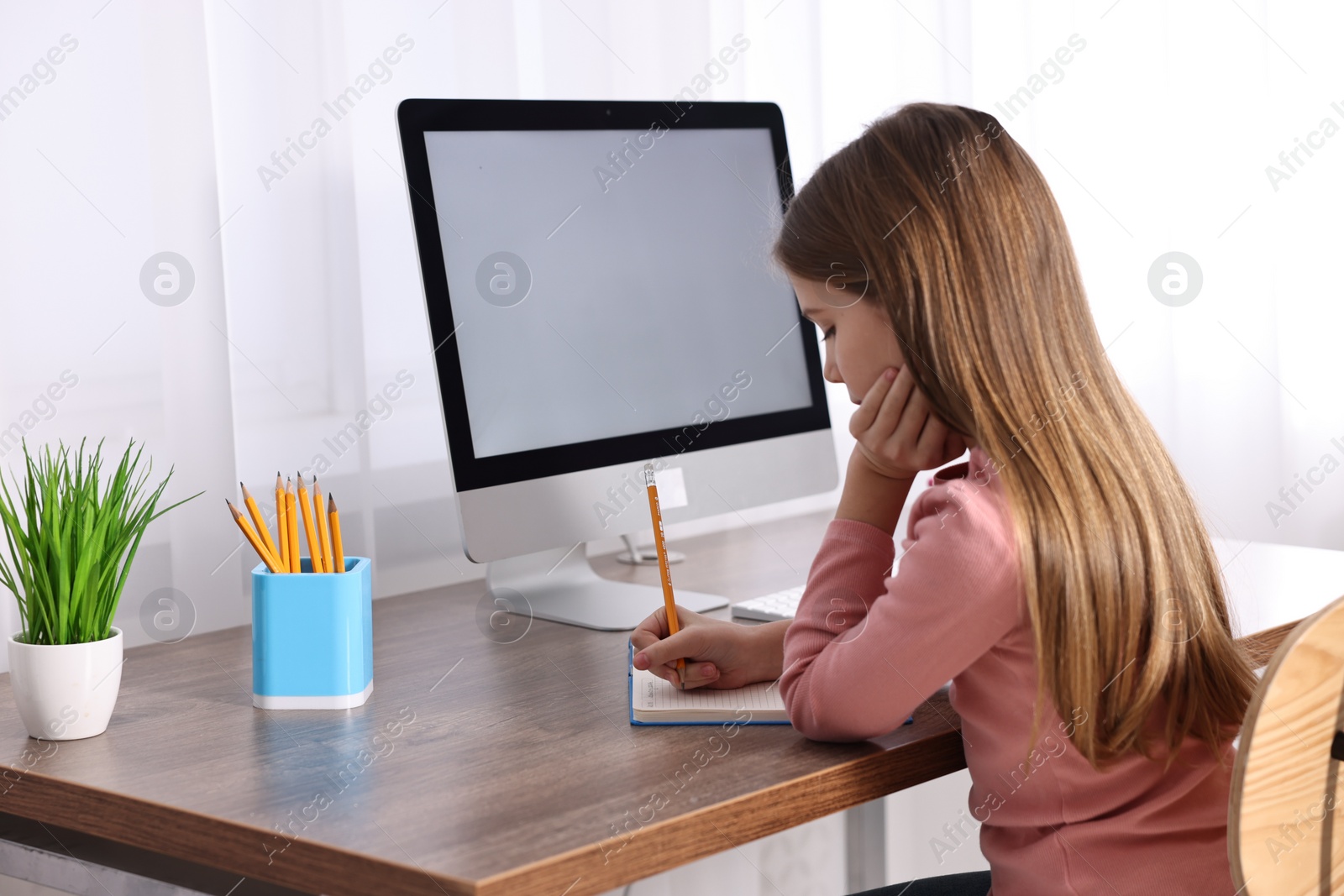 Photo of E-learning. Girl taking notes during online lesson at table indoors