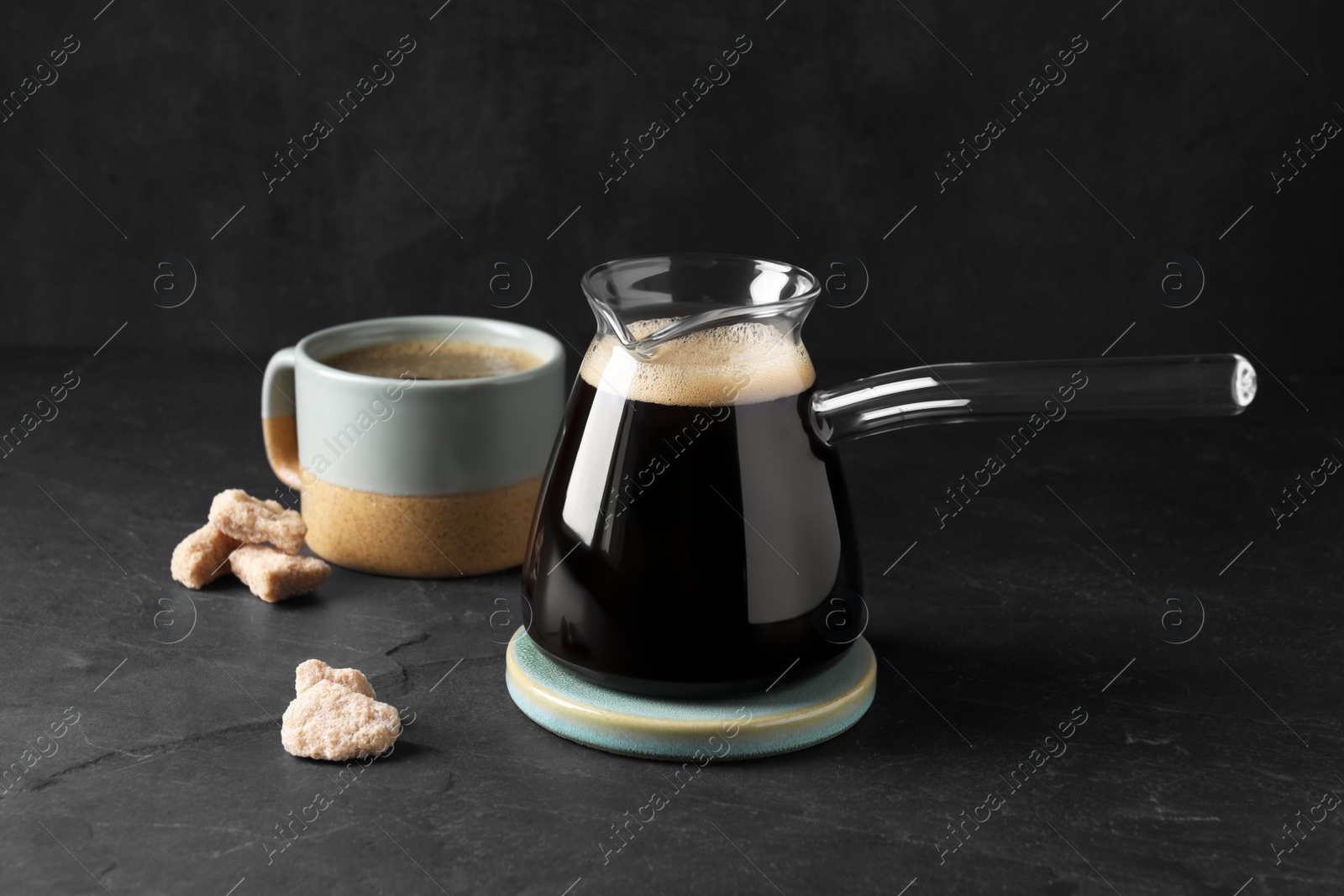 Photo of Turkish coffee in glass cezve and cup on dark grey table