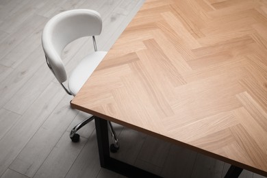 Photo of Wooden table near white office chair indoors, closeup