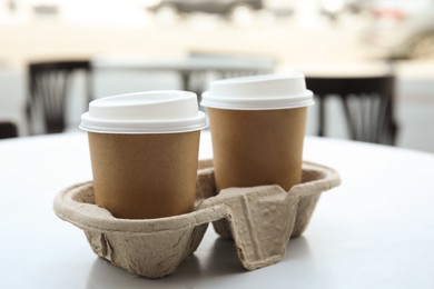 Photo of Takeaway paper coffee cups with plastic lids in cardboard holder on table outdoors