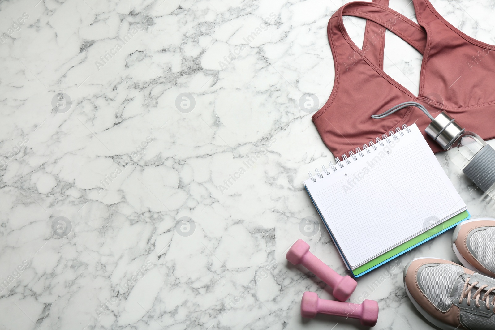 Photo of Flat lay composition with sportswear, notebook and dumbbells on white marble background, space for text. Gym workout plan