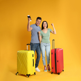 Happy couple with suitcases for summer trip on yellow background. Vacation travel
