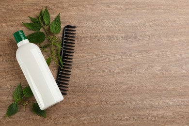 Photo of Stinging nettle, cosmetic product and comb on wooden background, flat lay with space for text. Natural hair care
