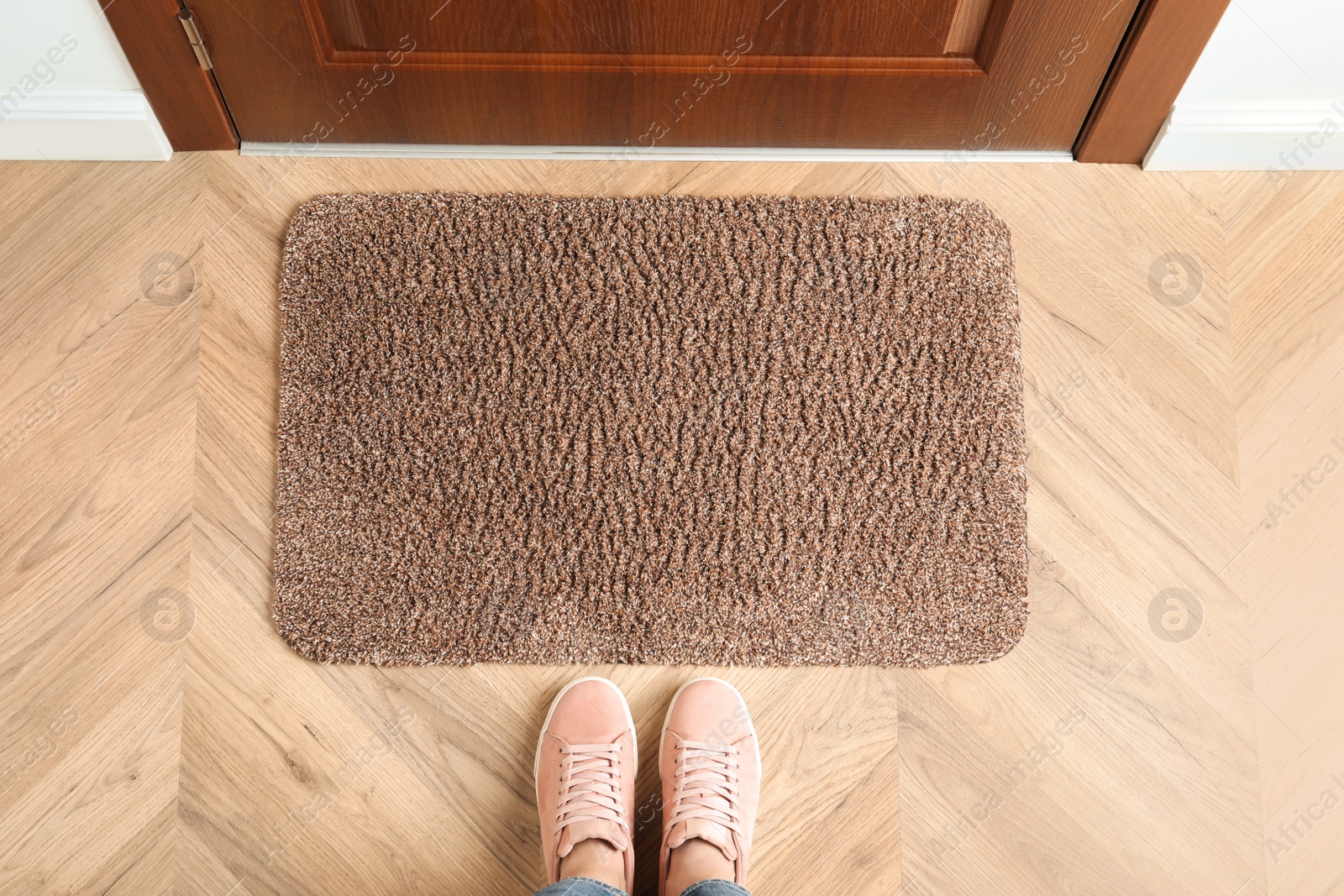 Photo of Woman standing near door mat on wooden floor in hall, top view