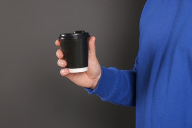 Photo of Man holding takeaway cup with drink on dark grey background, closeup. Coffee to go