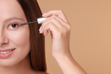 Photo of Woman applying serum onto eyelashes on beige background, closeup. Space for text