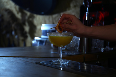 Photo of Bartender decorating glass of fresh alcoholic cocktail at bar counter, closeup