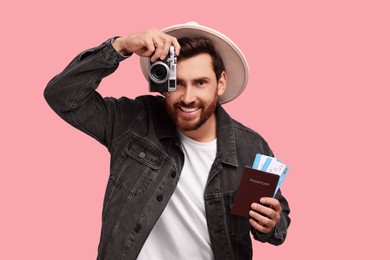 Smiling man with passport, tickets and camera on pink background