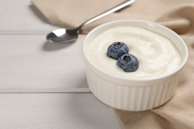 Bowl of yogurt with blueberries served on white wooden table, space for text