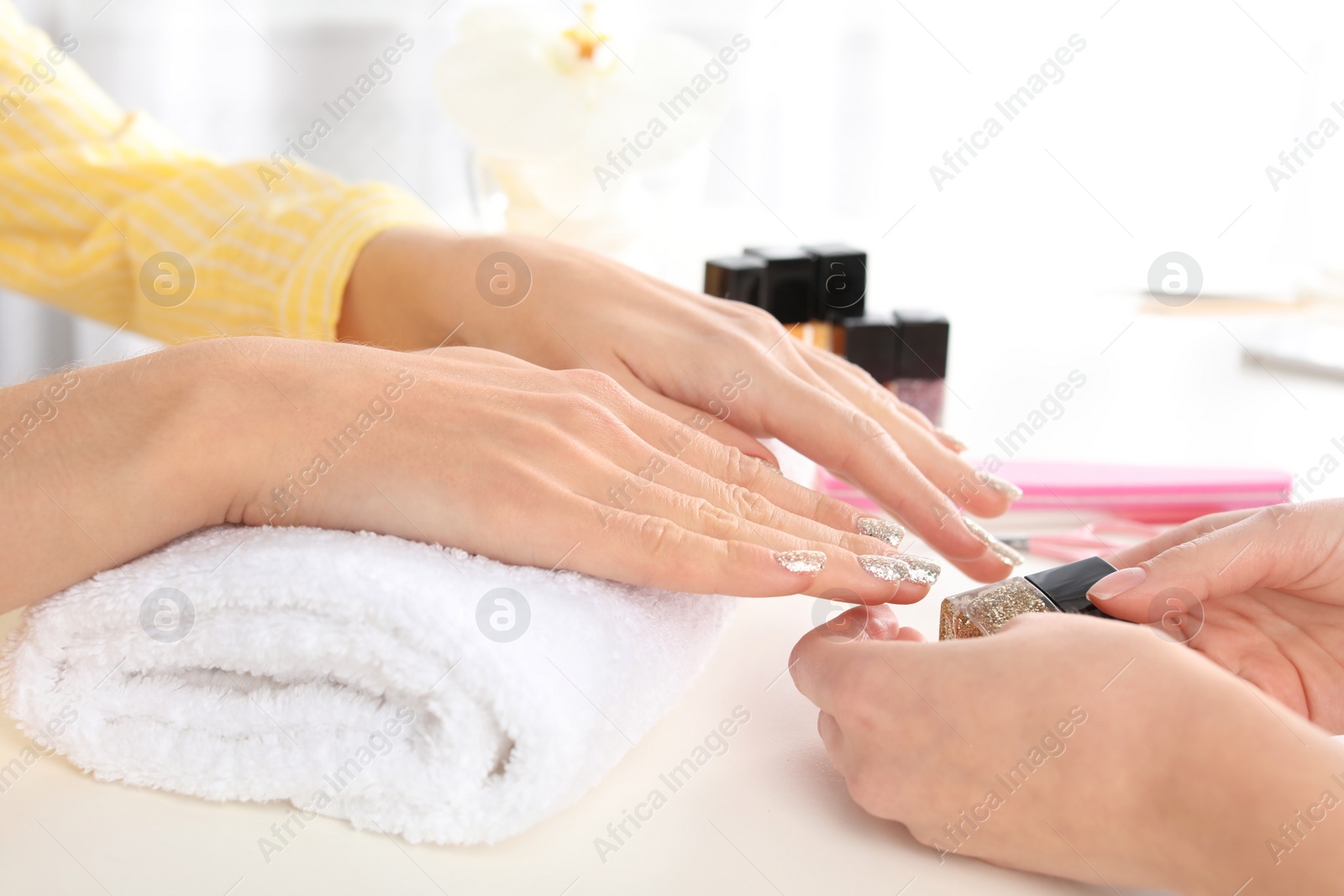 Photo of Client with shiny manicure and woman at table in salon, closeup. Nail polish trends