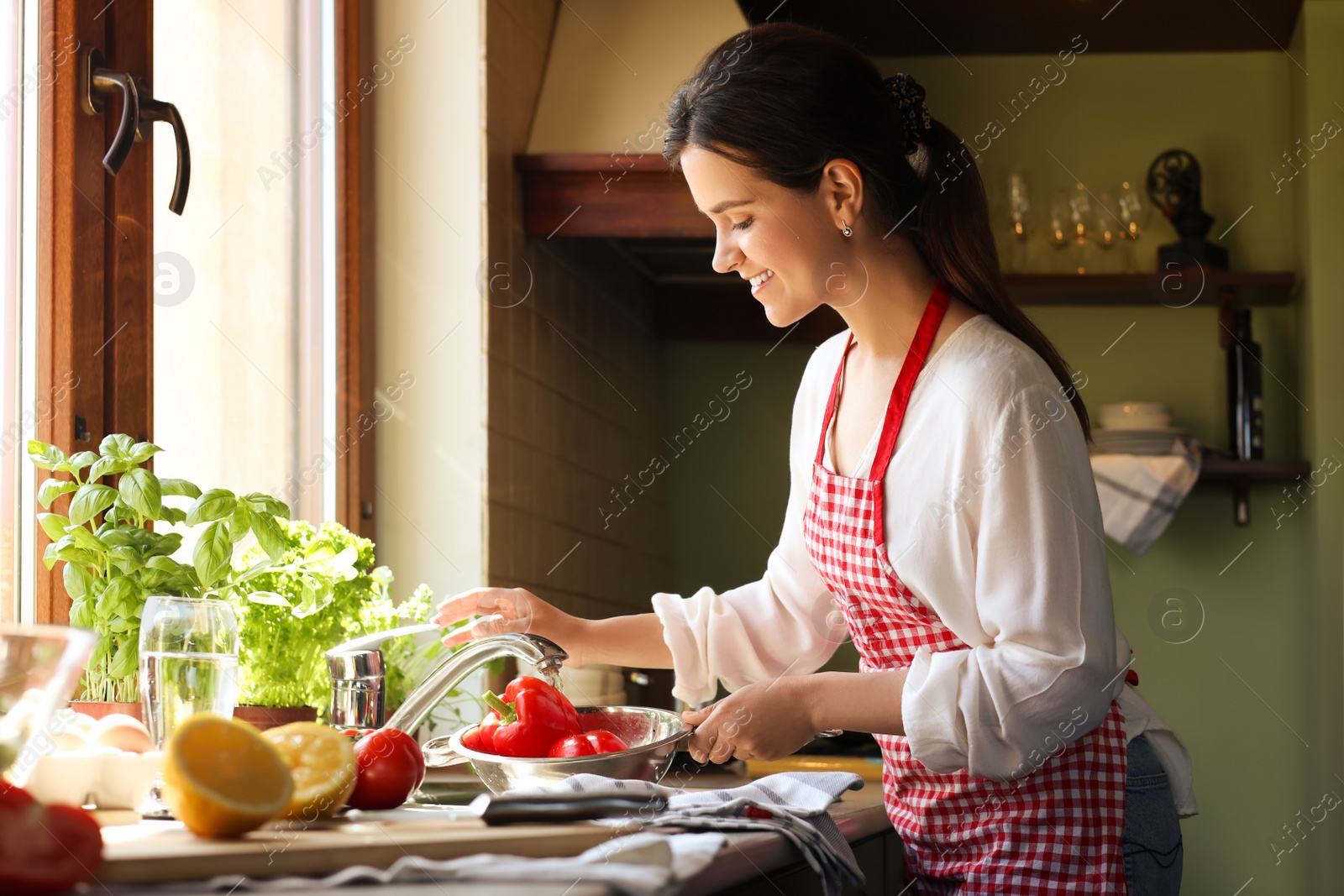 Photo of Young woman washing fresh bell peppers in kitchen sink