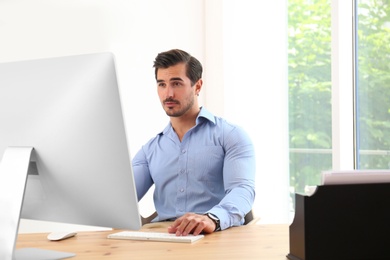 Handsome young man working with computer at table in office