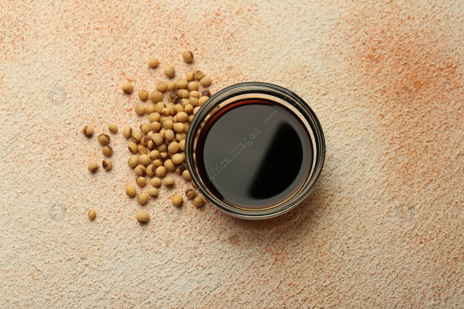 Photo of Soy sauce in bowl and beans on beige textured table, flat lay